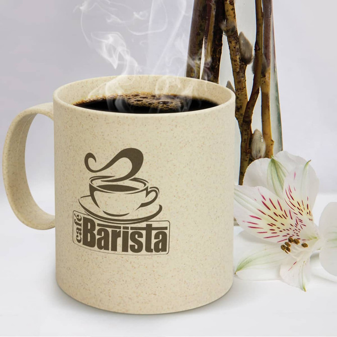 A cream-coloured coffee mug with a logo, filled with steaming coffee, beside a vase and a flower.