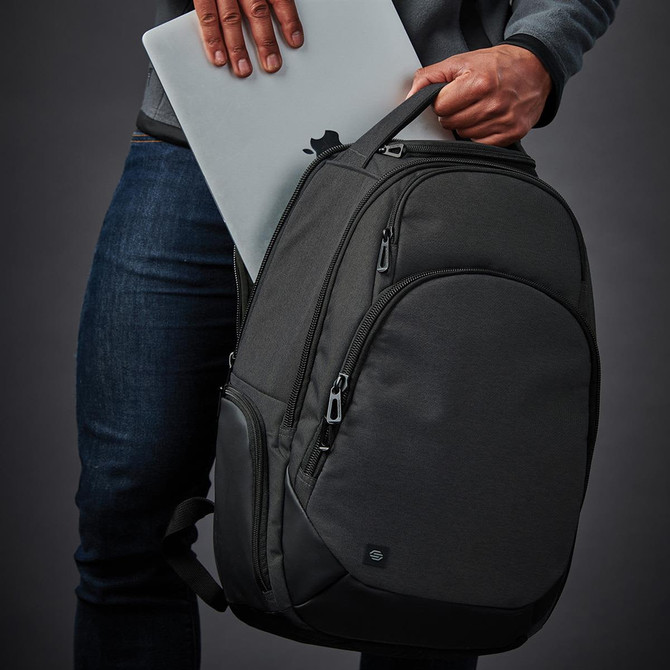 A grey backpack with multiple compartments, held by a person, with a laptop partially inserted. It has a logo.