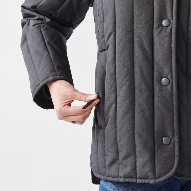 A thermal jacket in grey featuring a quilted design and a hand reaching into a side pocket. It has a logo.