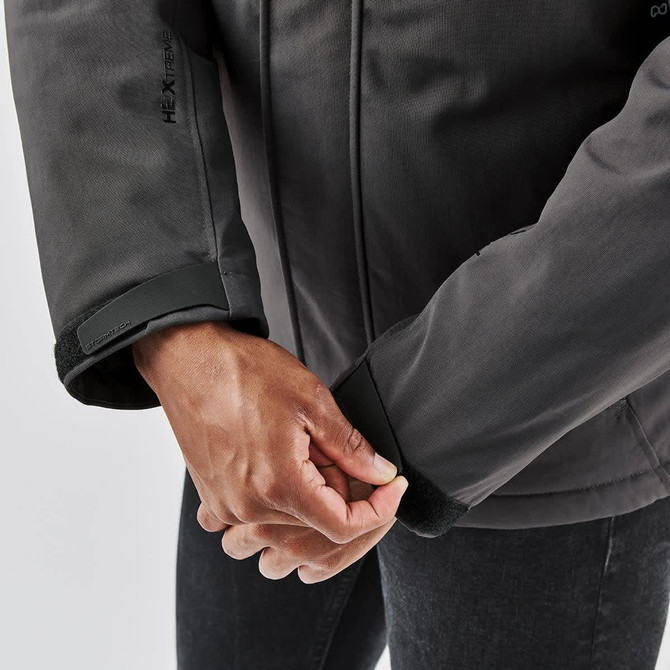 A close-up of a person's hands adjusting the cuffs of a dark grey thermal jacket, featuring a logo.