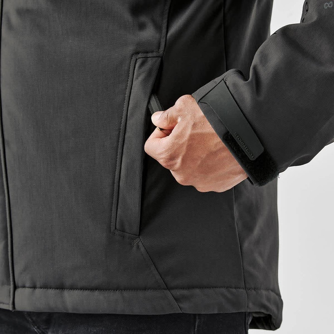 A black thermal jacket with a hand adjusting the pocket, featuring a logo on the sleeve.