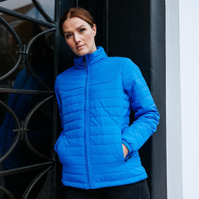 A blue women's quilted jacket with a high collar and two side pockets, modelled against a decorative door.