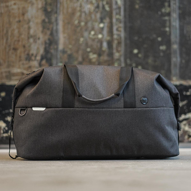A black duffle bag with rounded edges, featuring an exterior pocket and a logo.