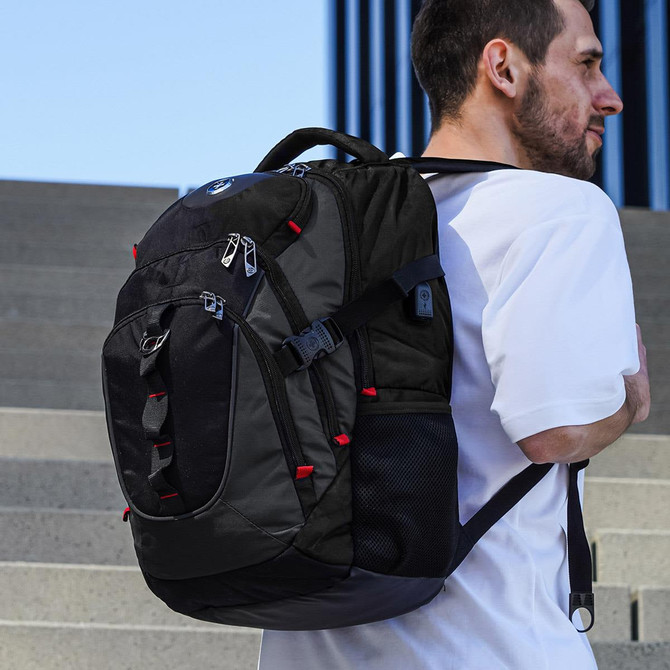 A black backpack with red accents is worn on the back of a person standing on steps, featuring multiple compartments and a logo.