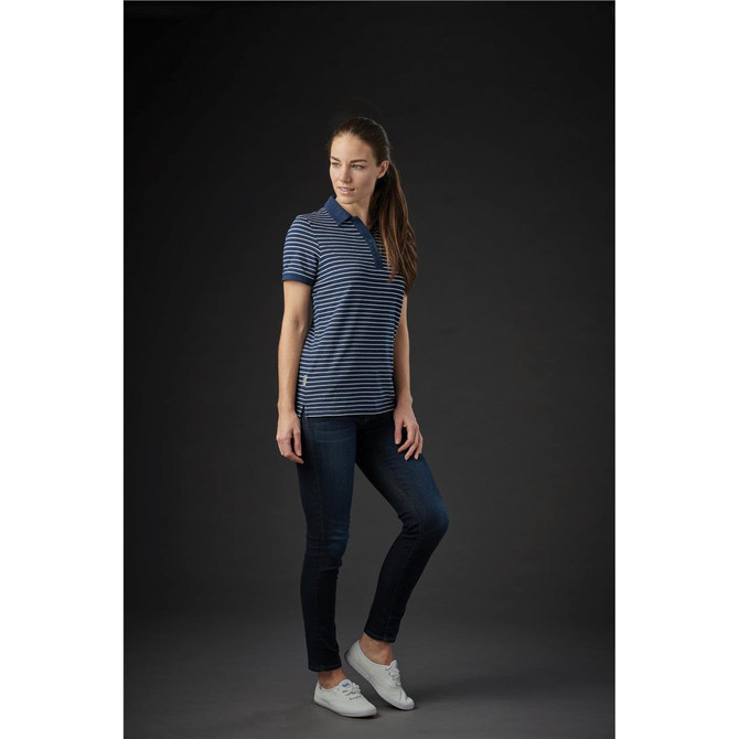 A woman wearing a navy and white striped polo shirt with a logo, paired with jeans and white shoes.