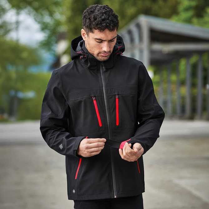 A black softshell jacket with red zippers and a hood, featuring a logo on one side.