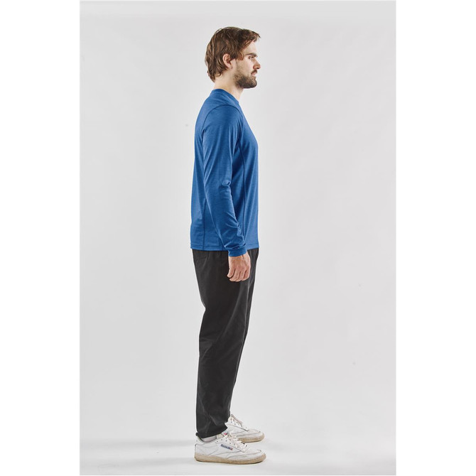 A man models a long-sleeve crew neck shirt in blue, paired with black pants. The shirt features a logo.