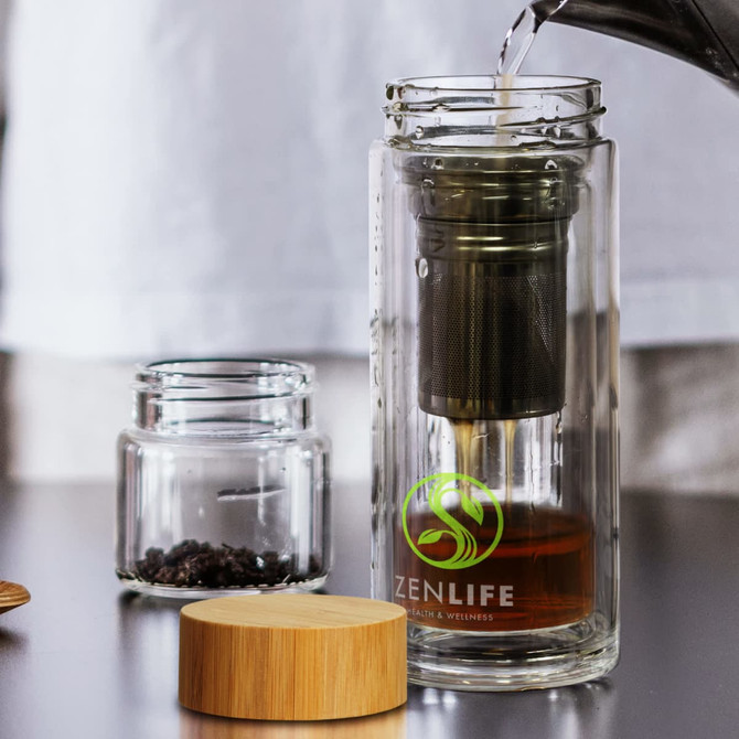 A drink bottle made of clear glass with a metal infuser, wooden lid, and a logo. Contains brewing tea.