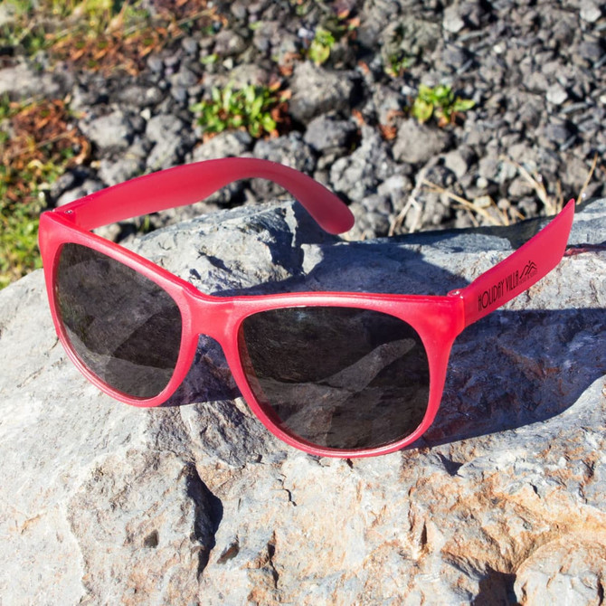 A pair of red sunglasses with dark lenses, resting on a rocky surface in a natural setting.