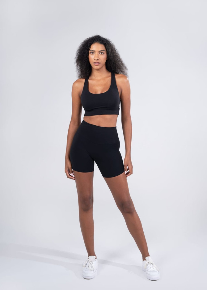 High rise legging shorts in black on a model, paired with a matching black crop top. The outfit features a logo.
