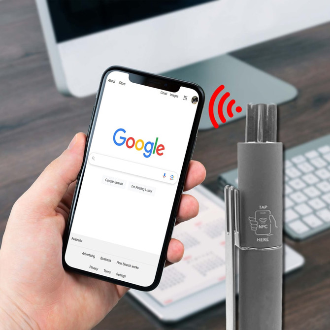 A grey metal pen with an NFC feature, placed beside a smartphone displaying a web search.