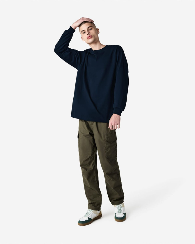 A model wearing a navy heavyweight cotton unisex long sleeve T-shirt paired with olive cargo pants and sneakers.