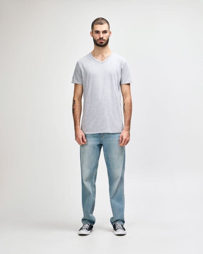 A man stands wearing a grey Gildan Softstyle V-Neck T-Shirt and light blue jeans, with a logo on the shirt.