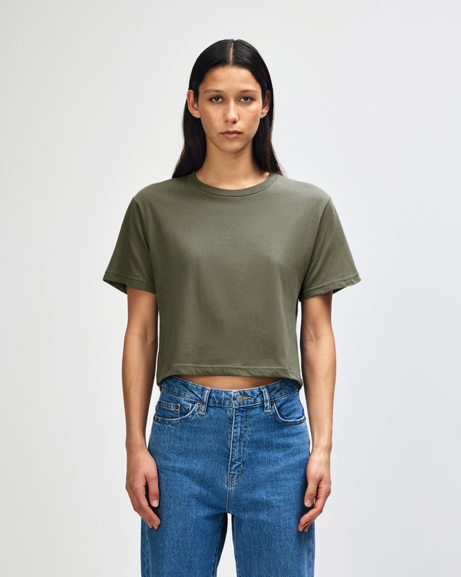 A women's boxy t-shirt in olive green, featuring a round neckline and short sleeves, styled with blue jeans.
