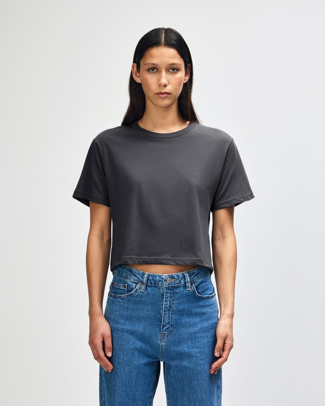 A women's boxy t-shirt in dark grey, featuring a round neckline and short sleeves, styled with high-waisted jeans.