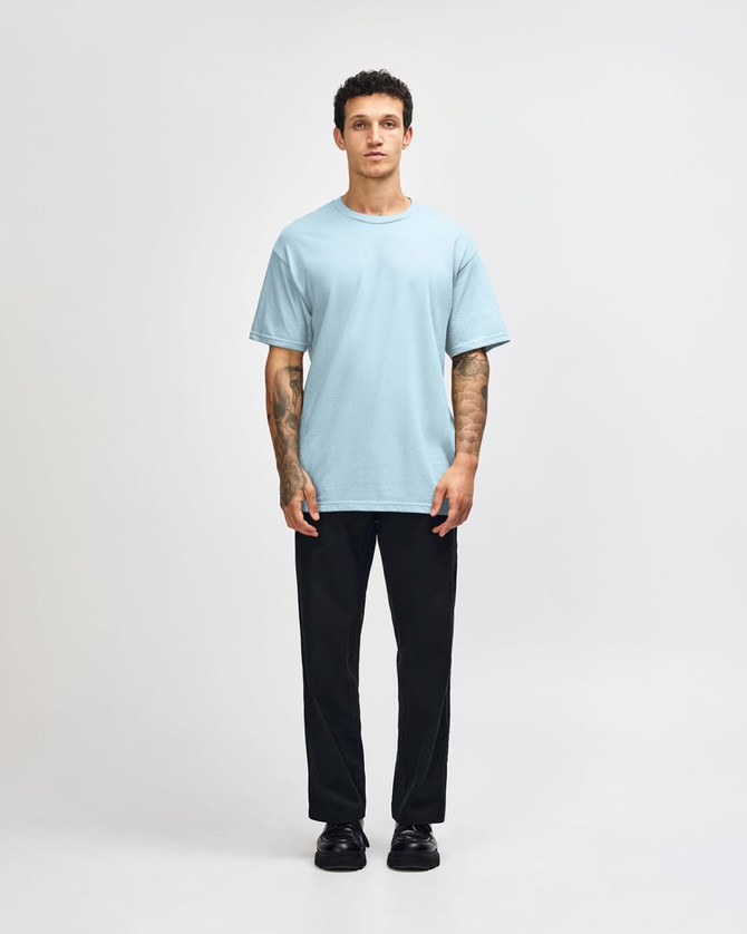 A light blue heavyweight cotton unisex T-shirt worn with baggy denim jeans, featuring a logo on the shirt.