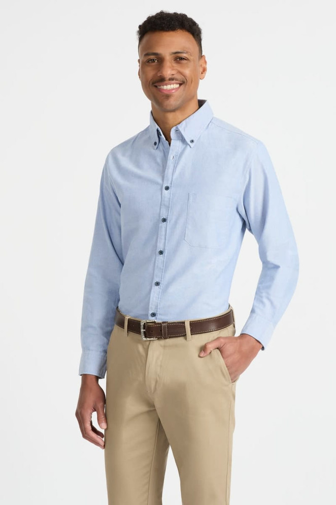 A light blue button-up shirt with long sleeves and a chest pocket, paired with beige trousers. The model is smiling and standing.