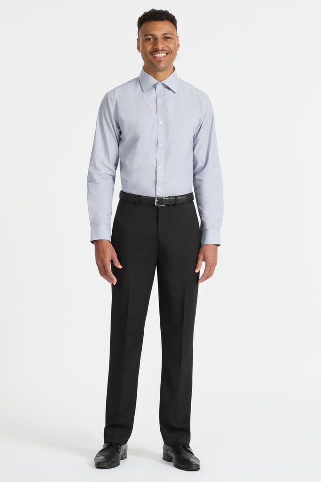 A man stands wearing a light blue long sleeve button-up shirt paired with black trousers and shoes. The shirt features a logo.