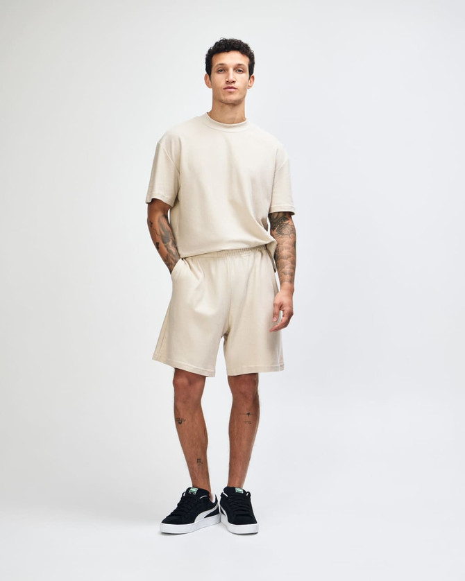 Beige unisex pique gym shorts displayed on a model, paired with a matching short-sleeve top and black sneakers.