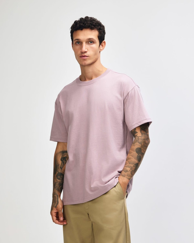 A model wearing a purple American Apparel Super Heavyweight T-Shirt, featuring short sleeves and a relaxed fit.