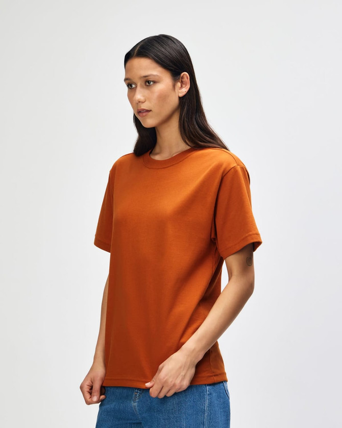 An orange Super Heavyweight T-Shirt displayed on a model, featuring a simple design and a branded logo.