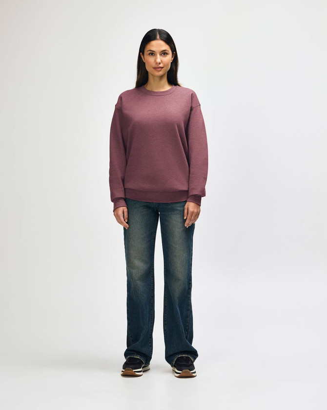 A woman stands wearing a maroon Gildan Heavy Blend hooded sweatshirt and blue jeans, showcasing a casual style.