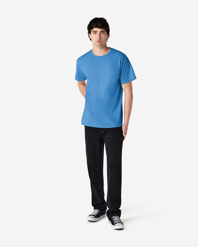 A adult t-shirt in light blue worn by a person, accompanied by black pants and sneakers. The shirt features a logo.