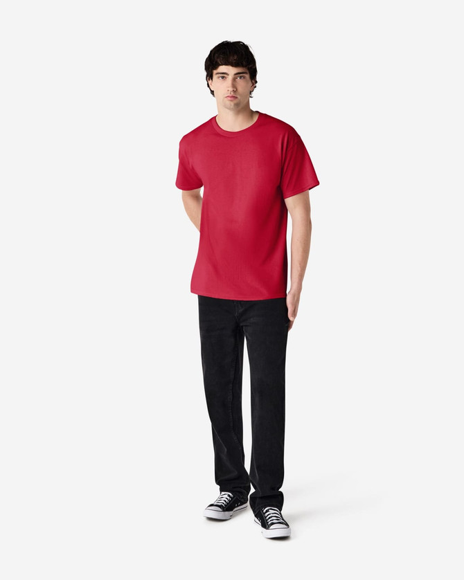 A red Gildan Ultra Cotton adult T-shirt displayed on a model wearing black jeans and sneakers. It features a logo.
