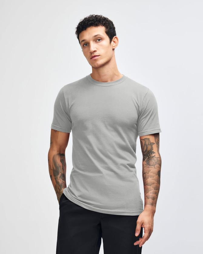 A grey unisex short sleeve T-shirt displayed on a model with hands in pockets, featuring a simple design.
