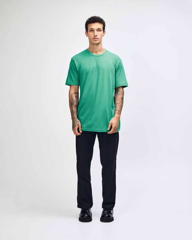 A model wearing a turquoise unisex fine jersey short sleeve t-shirt paired with khaki pants. The shirt has a logo.