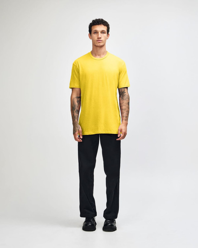 A model wearing a yellow unisex short sleeve T-shirt with black cargo pants and green and white shoes, featuring a logo.