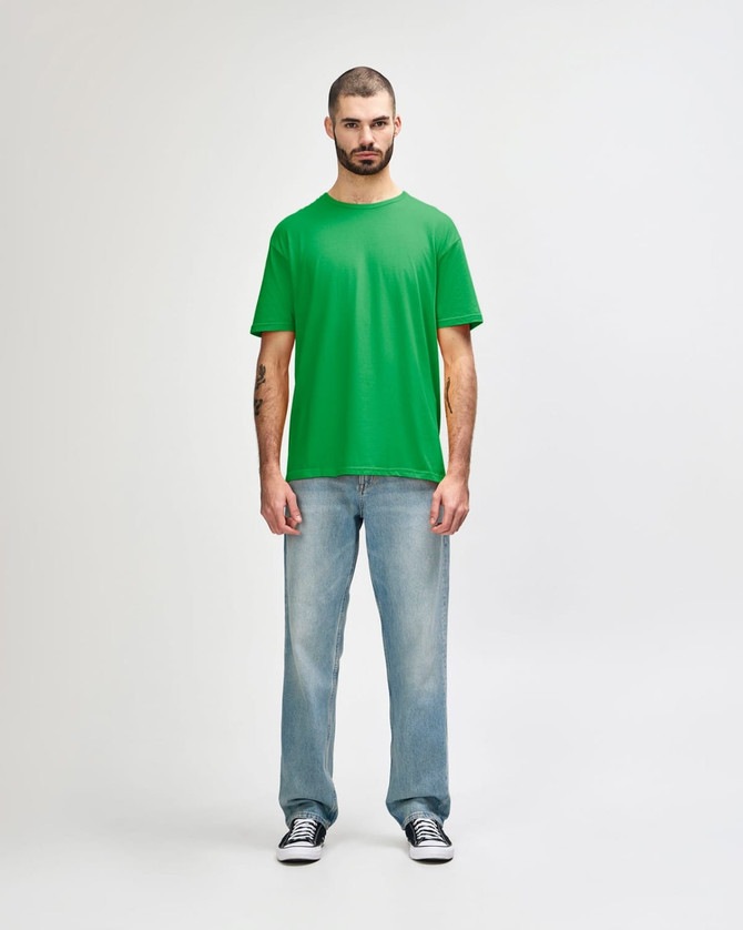 A green Gildan Softstyle adult T-shirt displayed on a model, paired with blue jeans and white shoes.