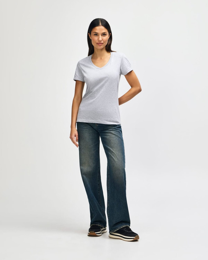 A grey ladies' V-neck T-shirt displayed on a model, paired with dark jeans and casual shoes.
