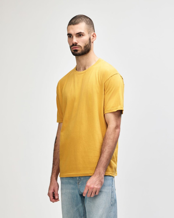 A mustard-coloured Gildan Softstyle adult midweight T-shirt displayed on a model, featuring a logo.