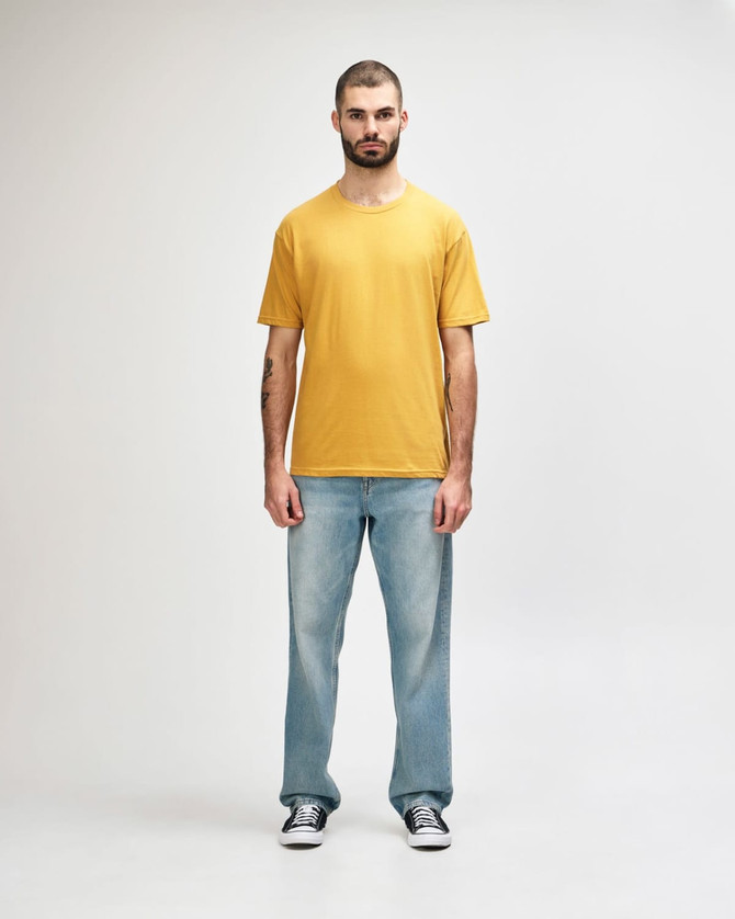 A man wearing a mustard yellow Gildan Softstyle adult midweight t-shirt and black jeans, walking casually.