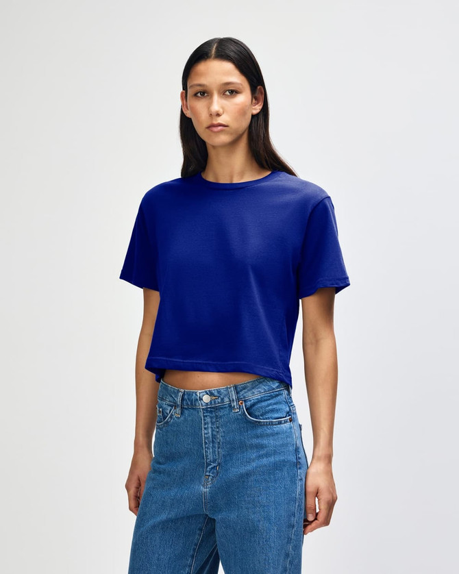 A blue boxy T-shirt with short sleeves, displayed on a model wearing jeans. The shirt has a logo.