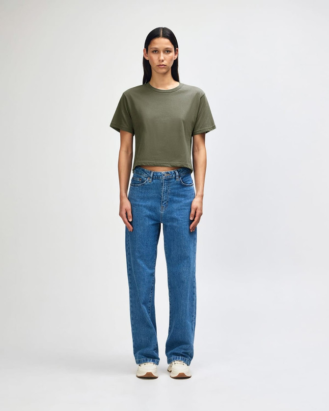 A woman stands wearing an olive green boxy t-shirt and light blue cargo jeans, paired with black and white sneakers.