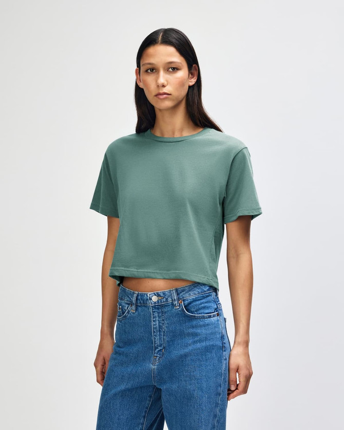 A model wearing a green boxy t-shirt, with short sleeves and loose fit, paired with light denim jeans.