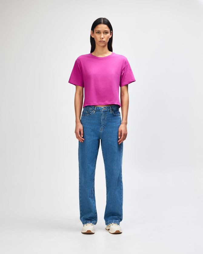 A boxy women's T-shirt in vibrant magenta, paired with light blue wide-leg jeans. The model stands with hands on hips.