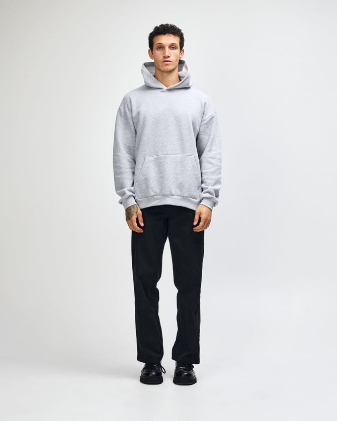 A unisex grey hooded sweatshirt with a kangaroo pocket, paired with light blue jeans and black sneakers.