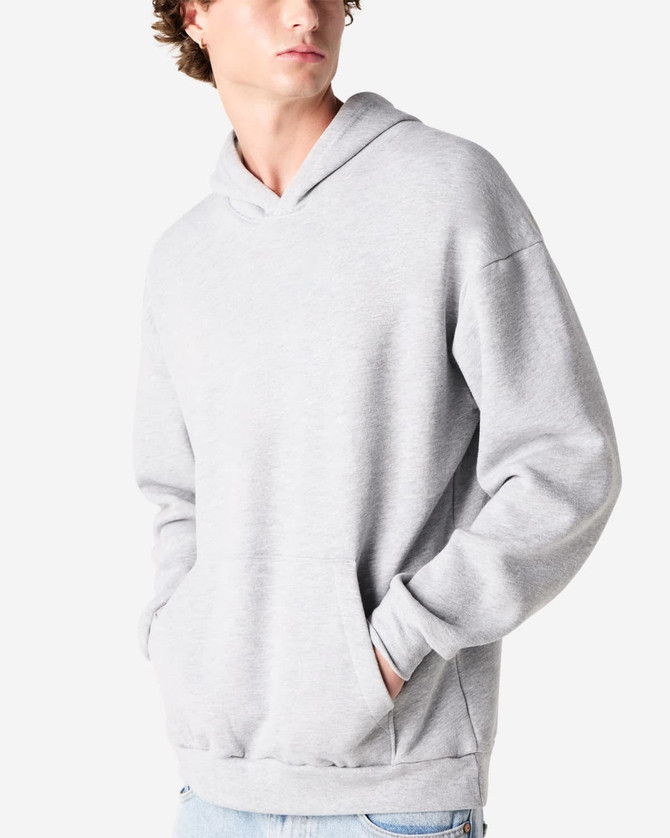 A grey unisex hooded sweatshirt with a front pocket and a logo. The model is standing with hands in pockets.