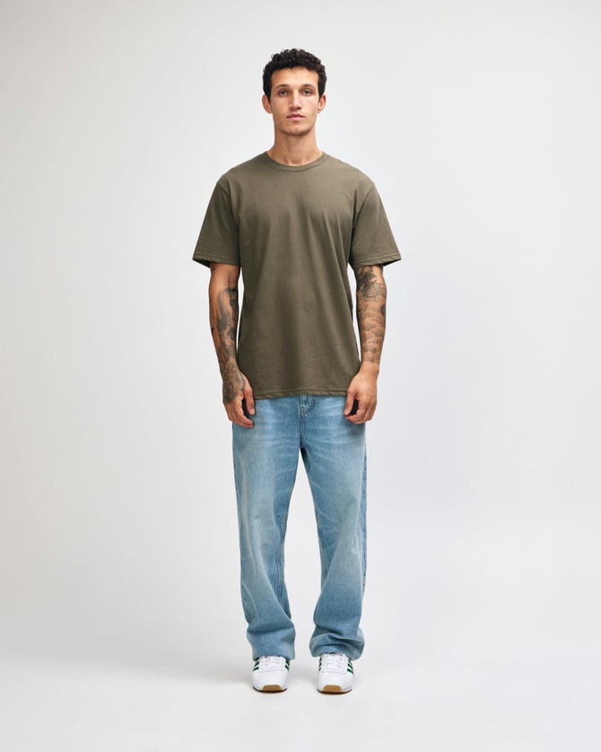 A model wearing an olive green unisex short sleeve T-shirt paired with black cargo pants and sneakers.