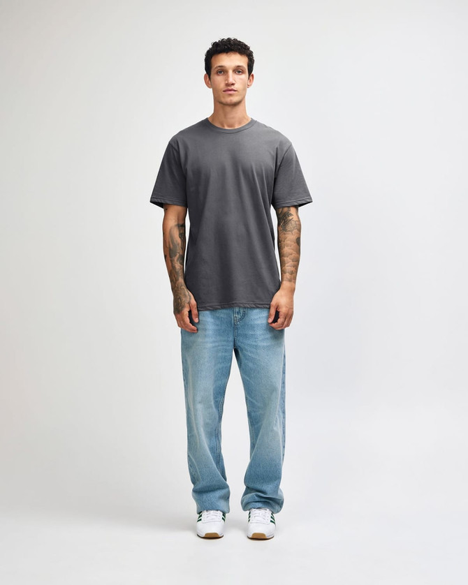 A grey unisex short sleeve t-shirt displayed on a model wearing light blue jeans and white shoes.