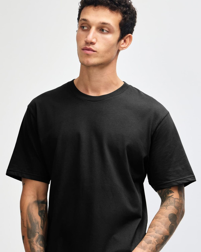 A black unisex short sleeve t-shirt displayed on a model with tattoos and a neutral expression.