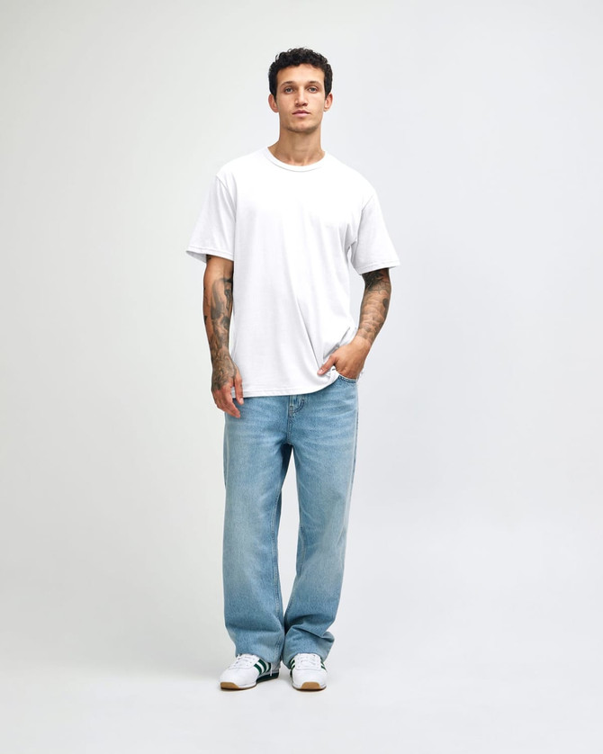 A man wearing a white sueded unisex short sleeve T-shirt and light blue jeans, standing against a neutral background.