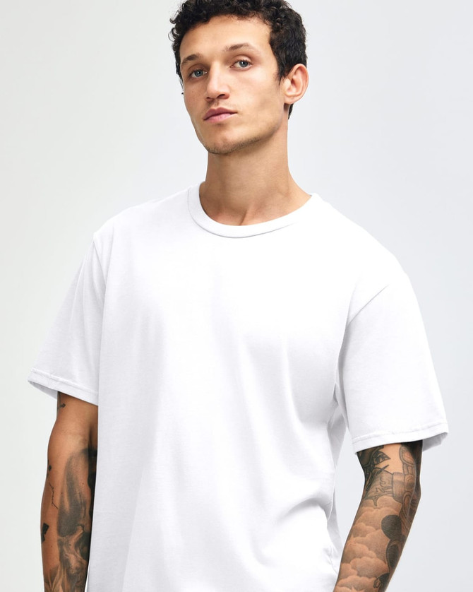 A white unisex short sleeve T-shirt on a model with tattoos, featuring a simple design and a logo.