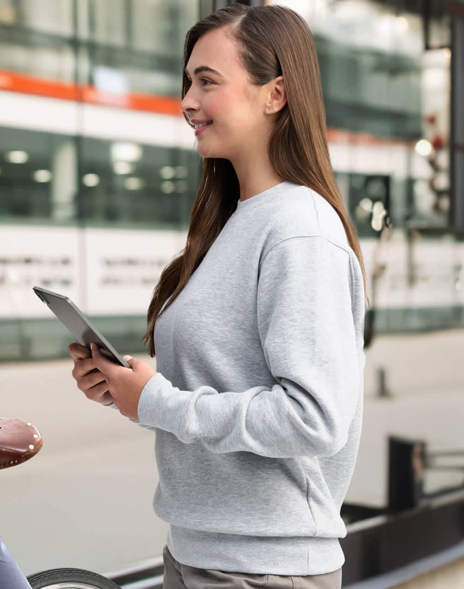 A grey crew fleece jumper, featuring a relaxed fit and long sleeves, is worn by a woman holding a tablet.
