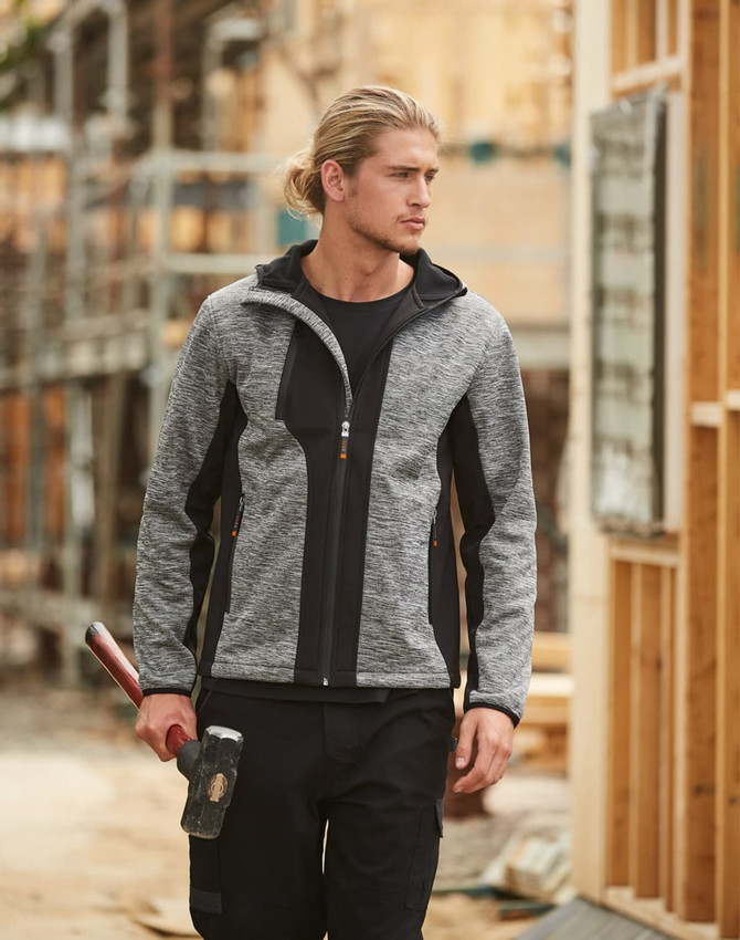 A grey and black workwear jacket with a hood, featuring a logo, worn by a male model in a construction setting.
