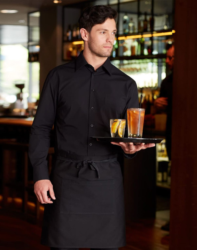 A man in a black cotton/poly stretch long-sleeve shirt holds a tray with drinks, wearing a matching black apron.