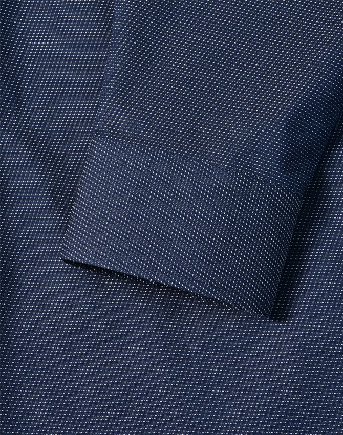 A close-up of a navy men's button-up shirt featuring a pin dot pattern and a cuff detail.